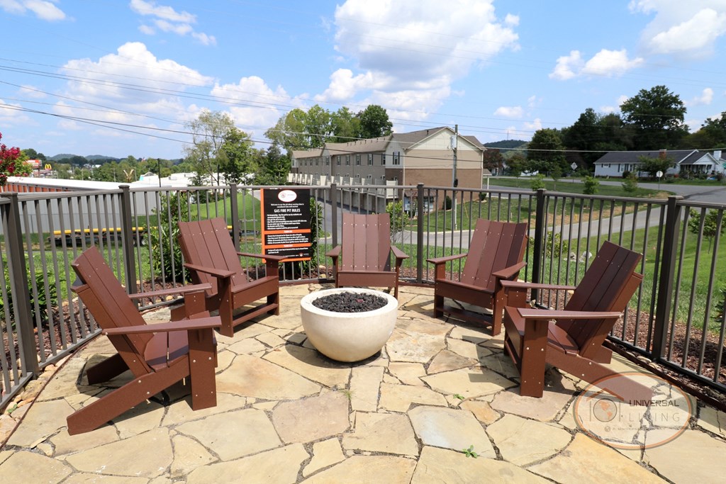 A fire pit on a stone patio with lounge chairs.