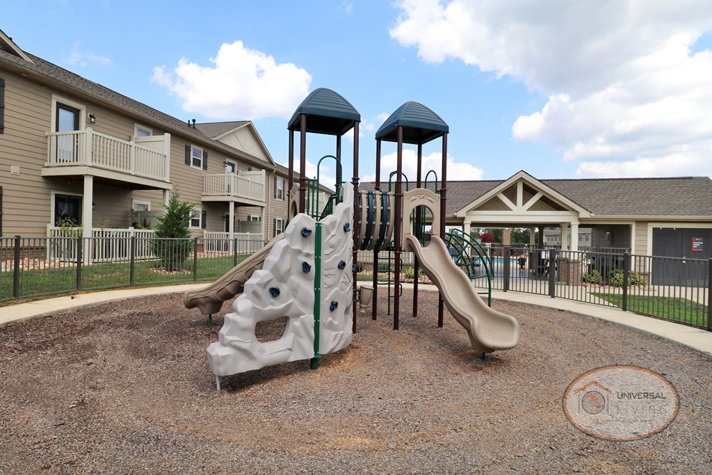 A fenced in playground with slide and jungle gym.