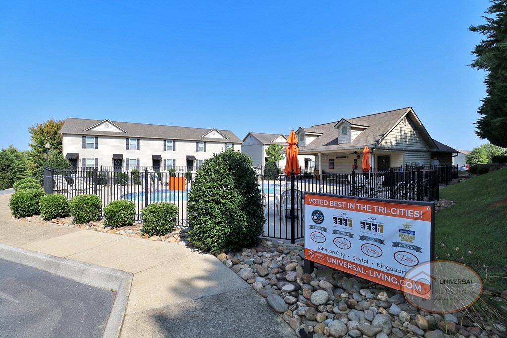 a sign is displayed in front of a white house with a fence and a yard