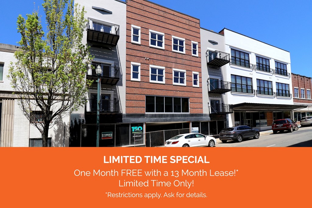 The front of a white and brick downtown apartment complex with balconies and large windows with an orange banner across the bottom that reads