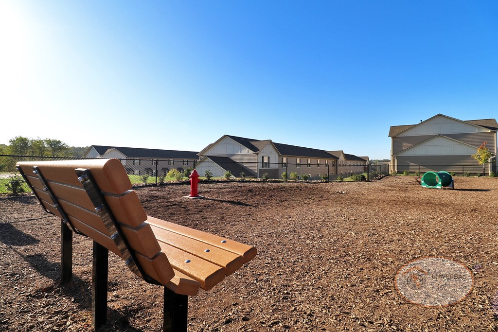 A view of the Bark Park from the inside with a bench, water fountain for dogs, and obstacles.
