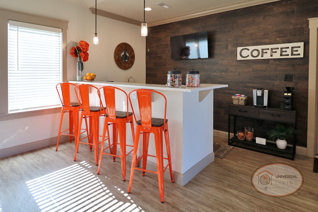 A coffee bar inside the clubhouse lounge with orange bar stool seating and a flat screen TV on a wood accent wall.