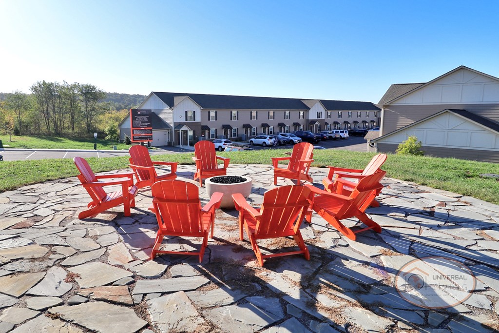 An outdoor fire pit on a stone patio surrounded by orange lounge chairs.