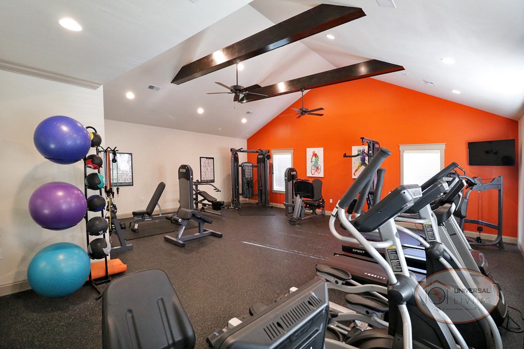 A resident fitness center with weight training and cardio equipment in front of an orange accent wall.