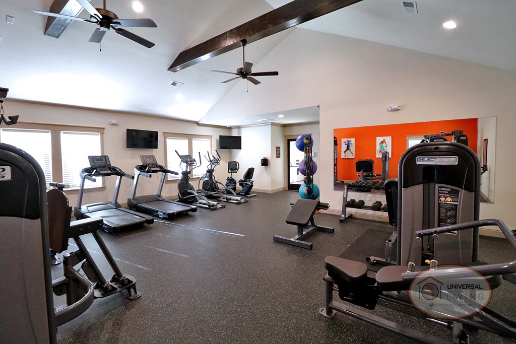 A fitness center with cardio and weight training equipment with a wall mirror and flat screen TVs.