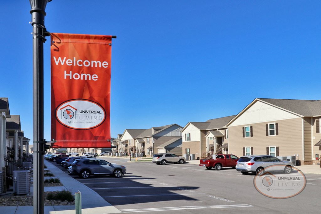 An orange sign that reads "Welcome Home" hangs above a row of tan apartment homes.