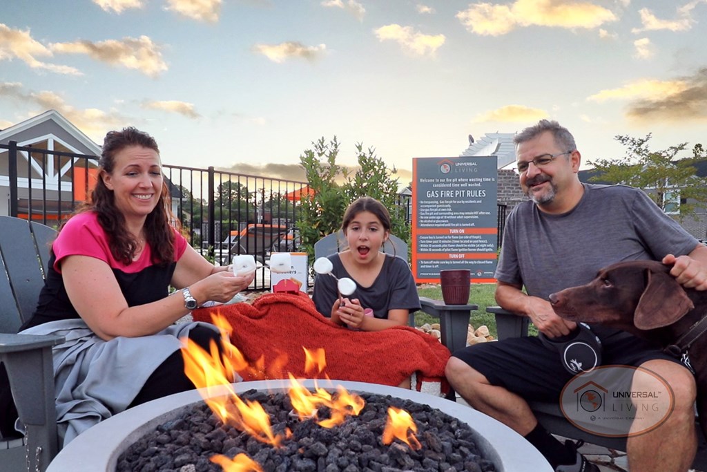 A family sitting around the fire pit with their dog, laughing and roasting marshmallows as the sun sets.