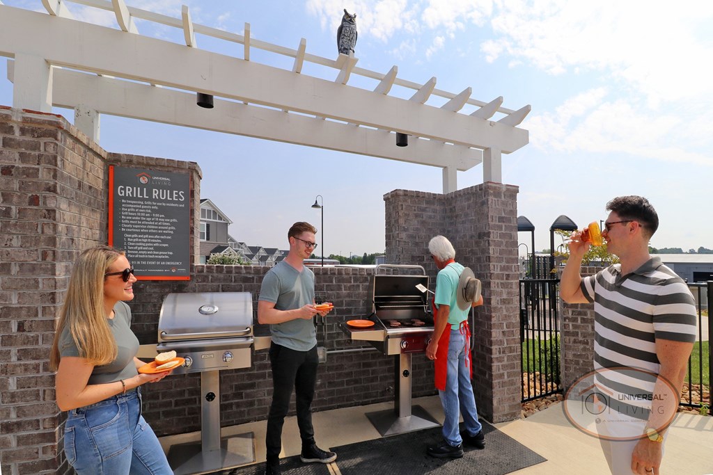 A group of friends gathered around the grills with their plates, waiting for burgers to finish cooking on the grill.