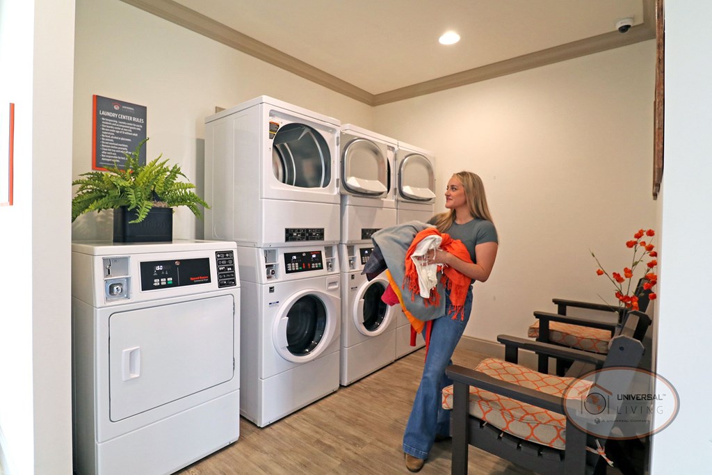 A woman holding an armful of laundry stands in front of an open washing machine.