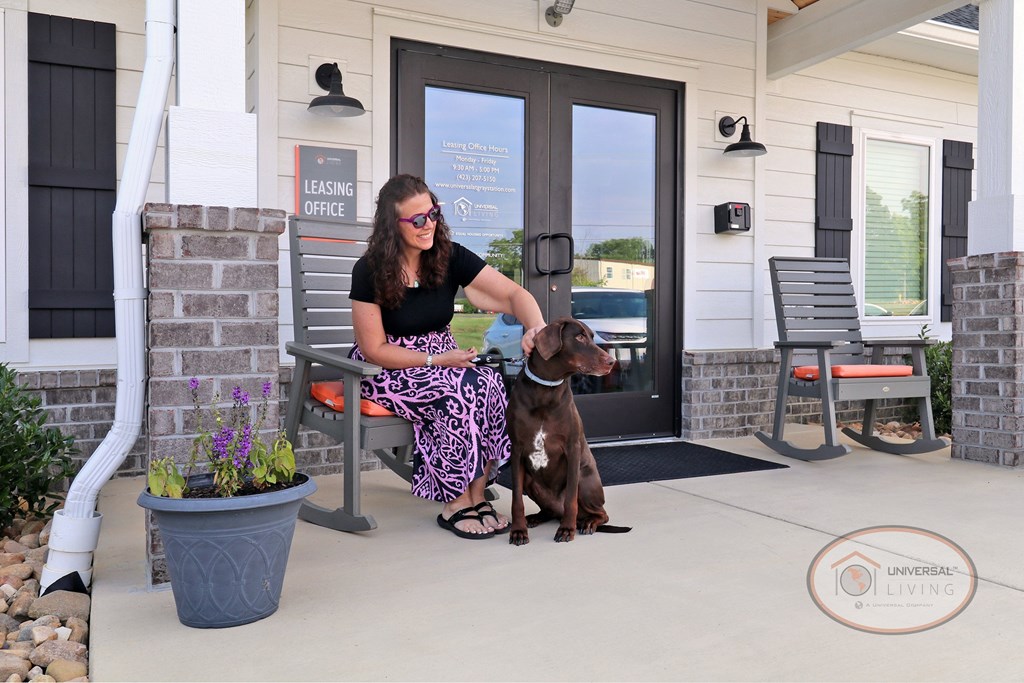 A woman sitting on a bench with her dog in front of the Clubhouse entrance.