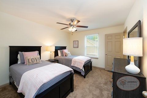 A bedroom with two twin beds, carpet, and a ceiling fan.
