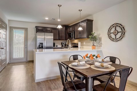 A kitchen with a table set for two with a clock on the wall.