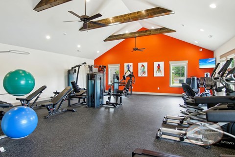 A fitness center with an orange accent wall, exposed beams, and weight lifting and cardio equipment.