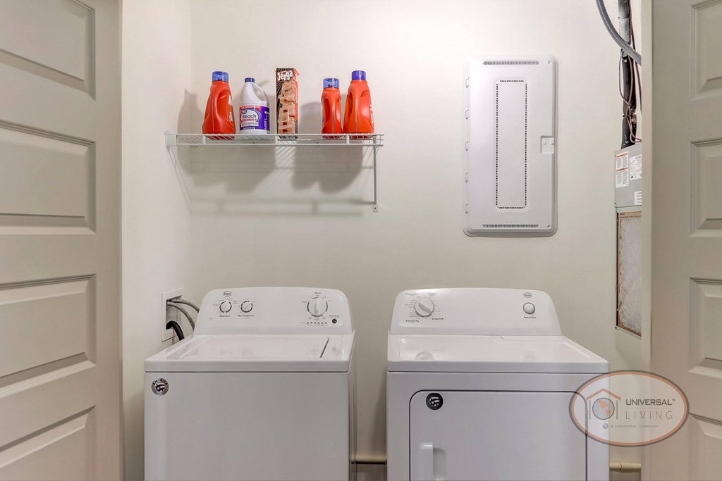 An in-unit laundry room with a washer and dryer and a shelf with bottles of detergent.