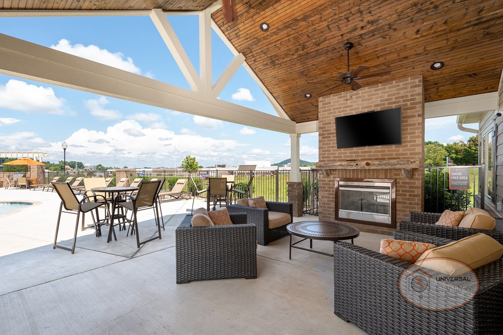 A poolside patio with fireplace, flat screen TV, and seating with a view of the pool and apartments in the background.