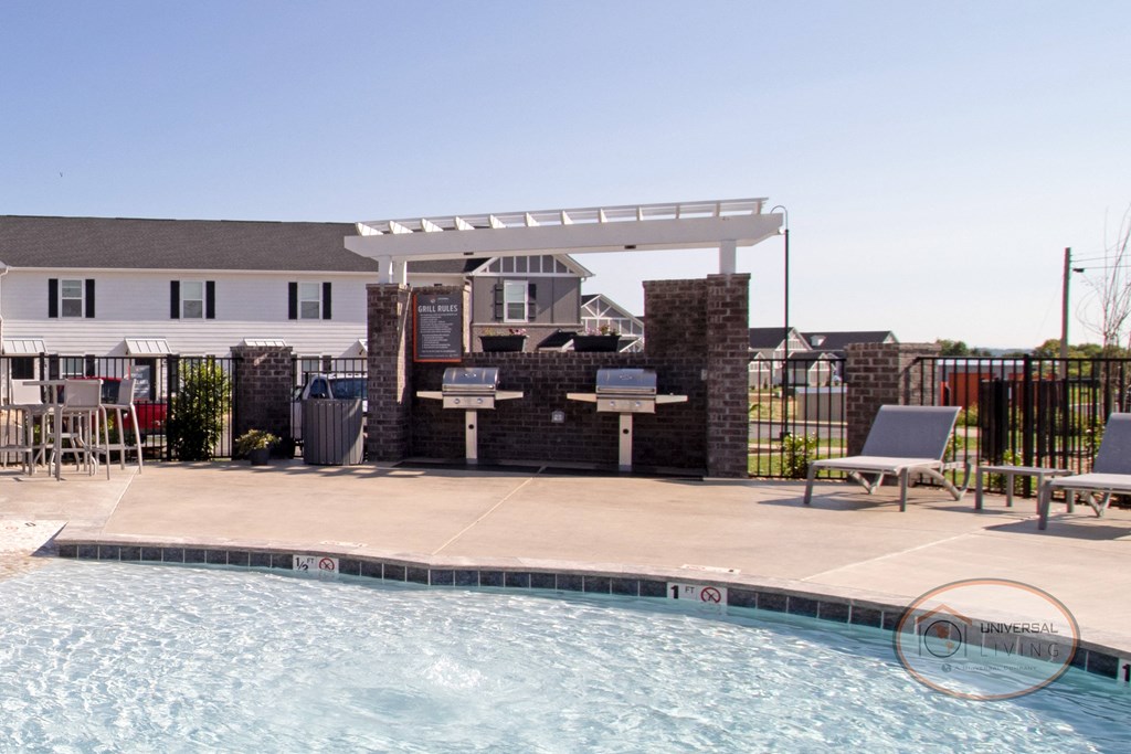 A grilling station with stainless steel grills, poolside lounge chairs, and a pool.