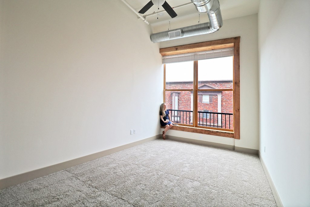 A woman sitting in an empty room looking out of a huge window.