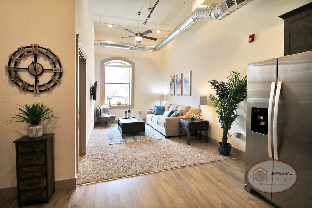 A living room with white walls, white carpet, furnished with a couch and stainless steel appliances.