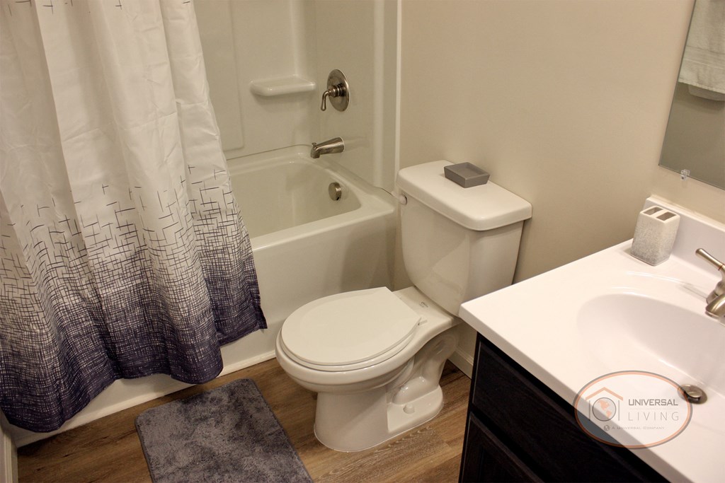 A bathroom with dark cabinets, white countertops, a shower over tub, sink, and toilet.