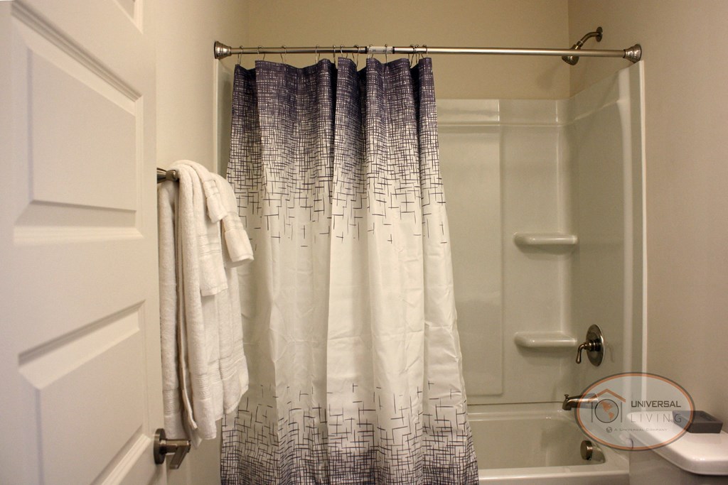 A bathroom with dark cabinets, white countertops, a shower over tub, sink, and toilet.