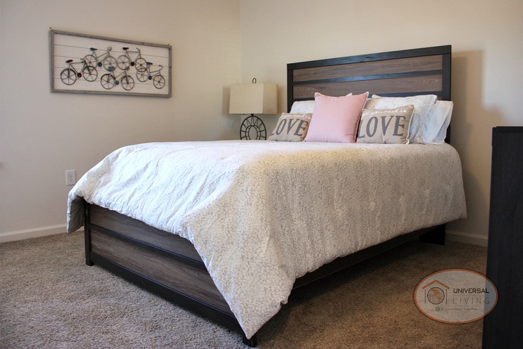 A bedroom with a large bed, dresser, carpet, and white walls.