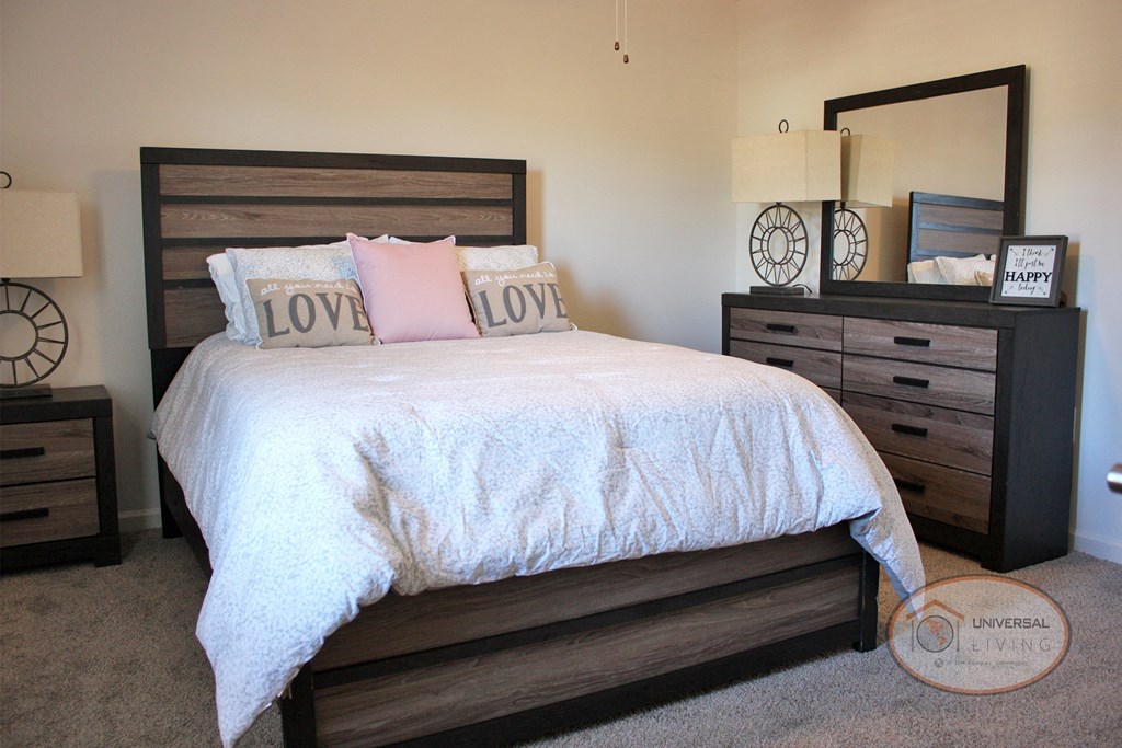 A bedroom with a large bed, dresser, carpet, and white walls.
