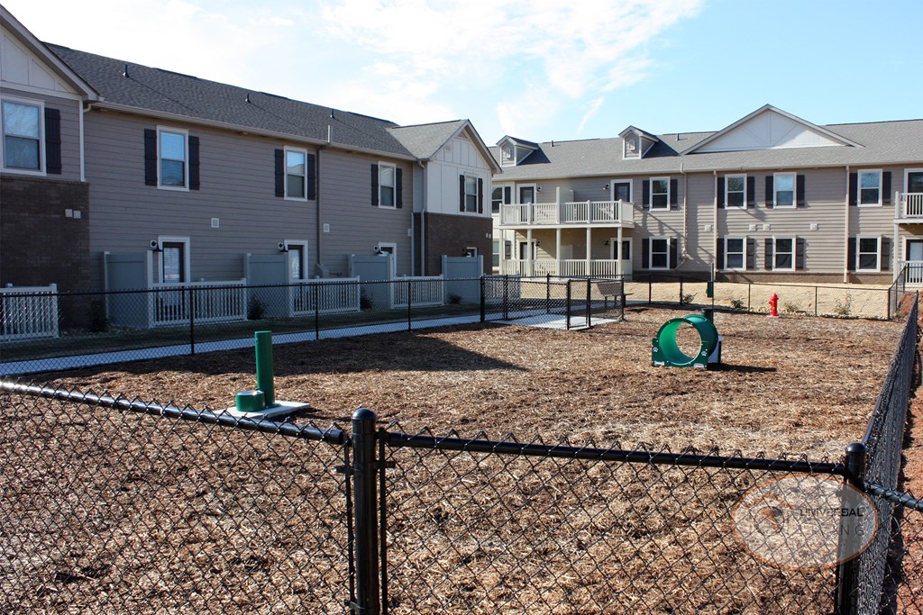 A fenced in dog park with fire hydrant, bench, and watering hole.
