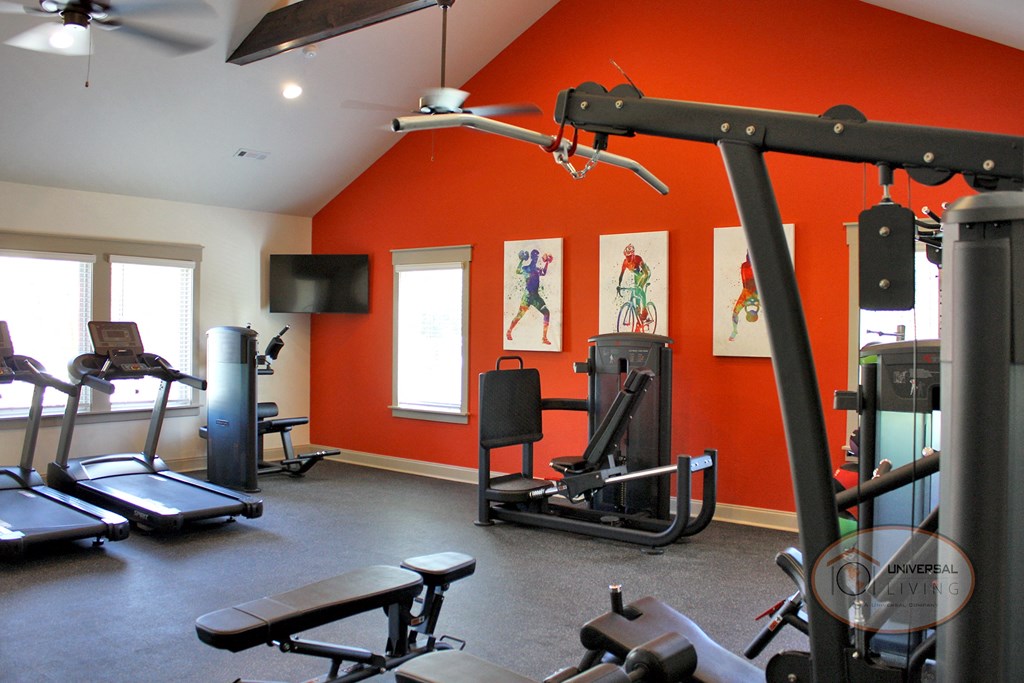 A fitness center with weight training and cardio equipment with an orange accent wall.