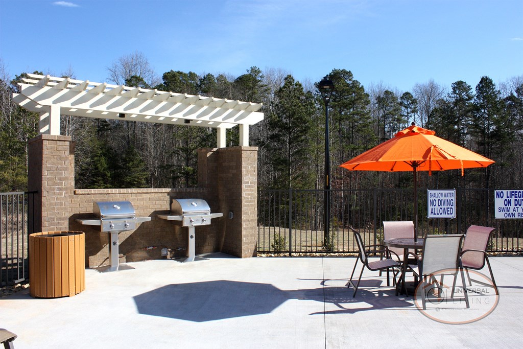 A grilling station with stainless steel grills, poolside lounge chairs, and a pool.