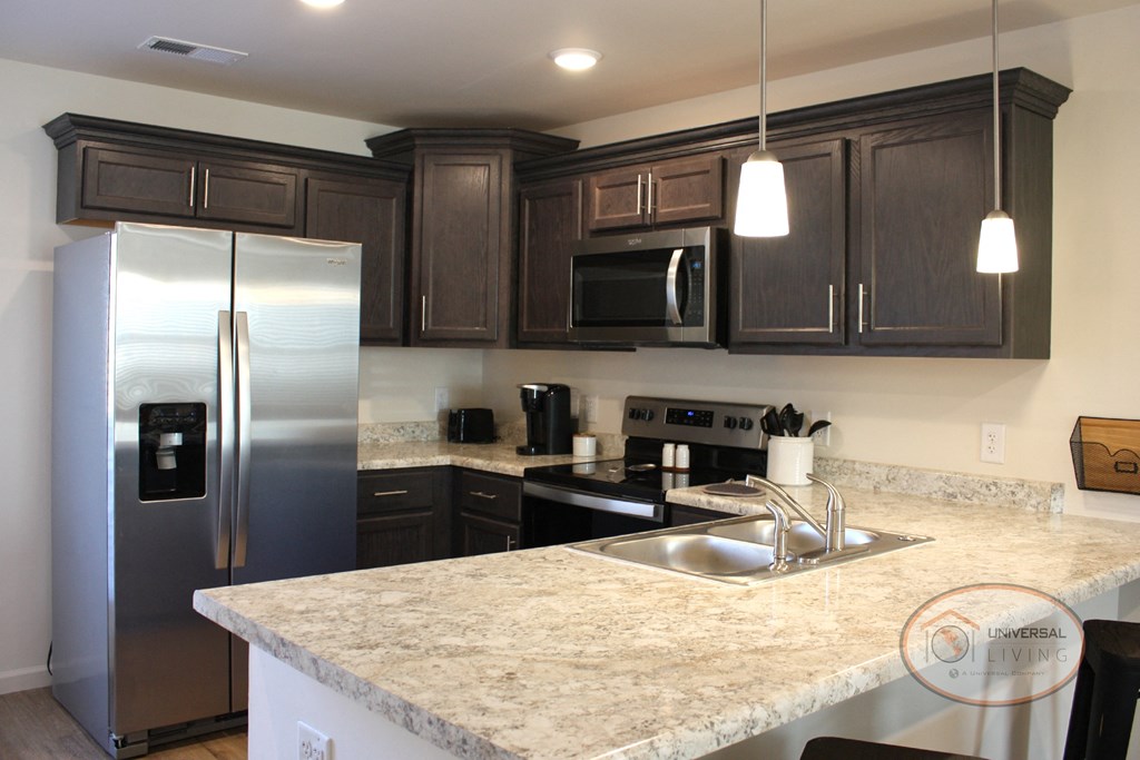A kitchen with light countertops, dark cabinets, and stainless steel appliances.
