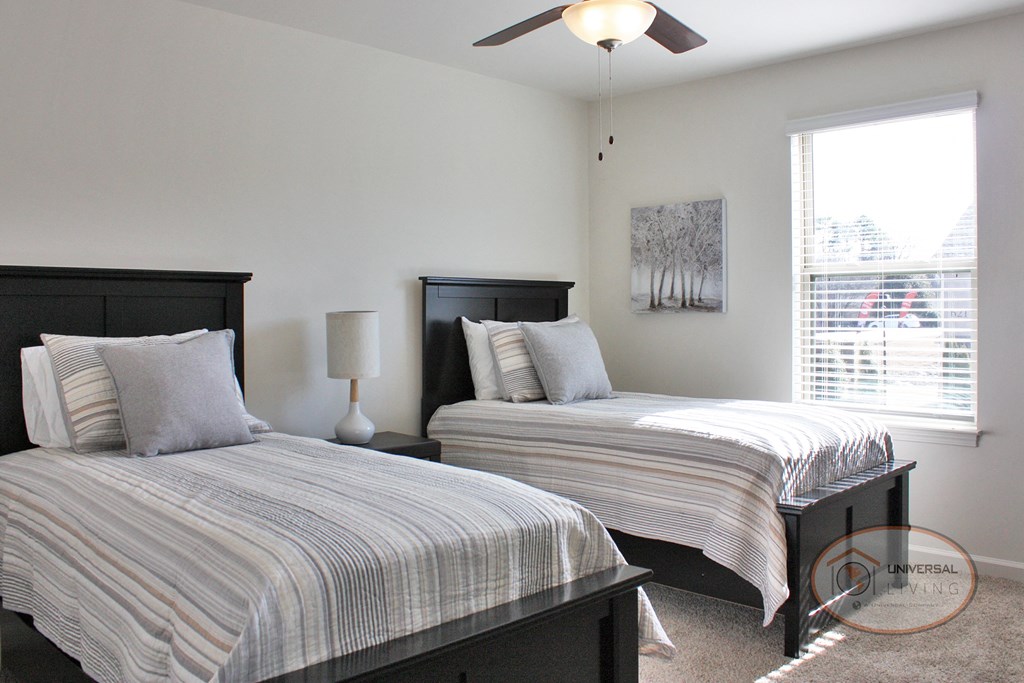 A bedroom with two twin beds, carpet, white walls, and a window.