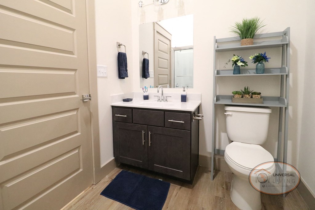 A bathroom with vinyl hardwood flooring,  dark cabinets, and white counters.