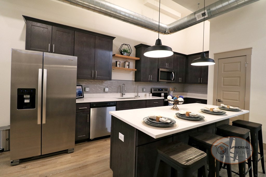 A kitchen with a large island and stainless steel appliances with dark cabinets and light counter tops.