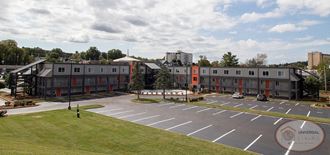Large, three story, grey apartment complex with orange accents. Apartment complex has a large parking lot and gated pool, located in the heart of Johnson City, TN.