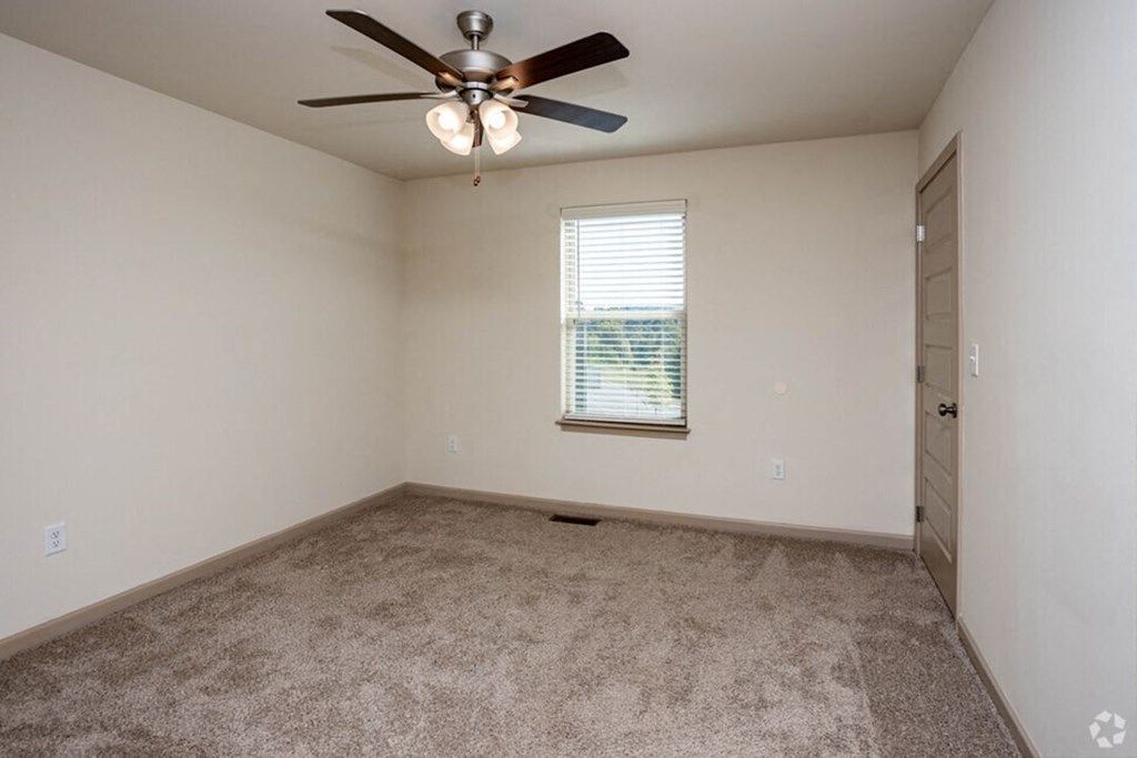 An empty bedroom with ceiling fan and carpet
