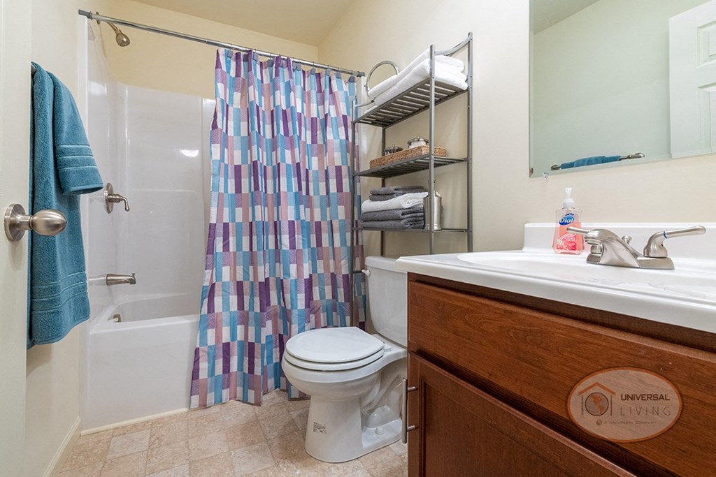 A bathroom with dark cabinets, white countertops, a shower over tub, sink, and toilet.