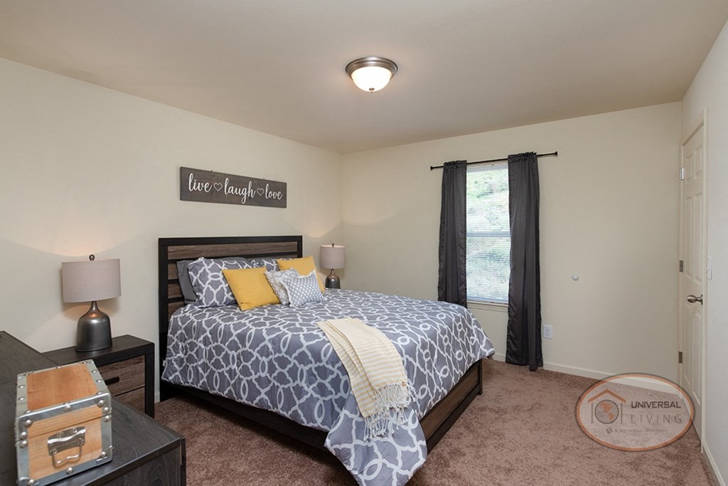 A bedroom with a large bed, dresser, carpet, and white walls.