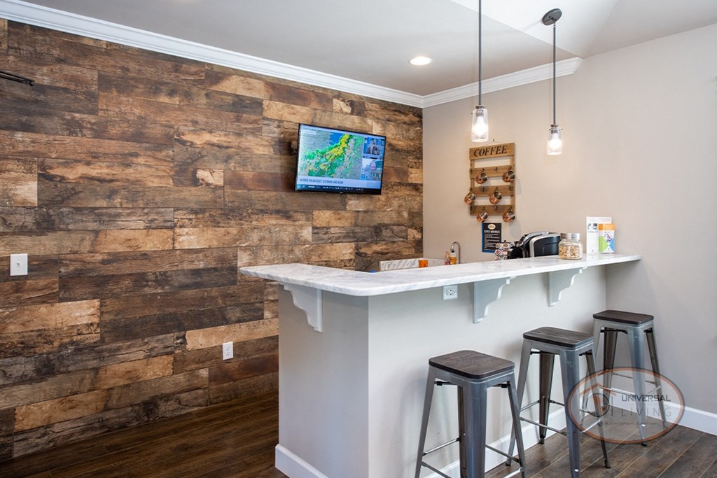 A coffee bar with flat screen TV, coffee machine, and barstool seating.