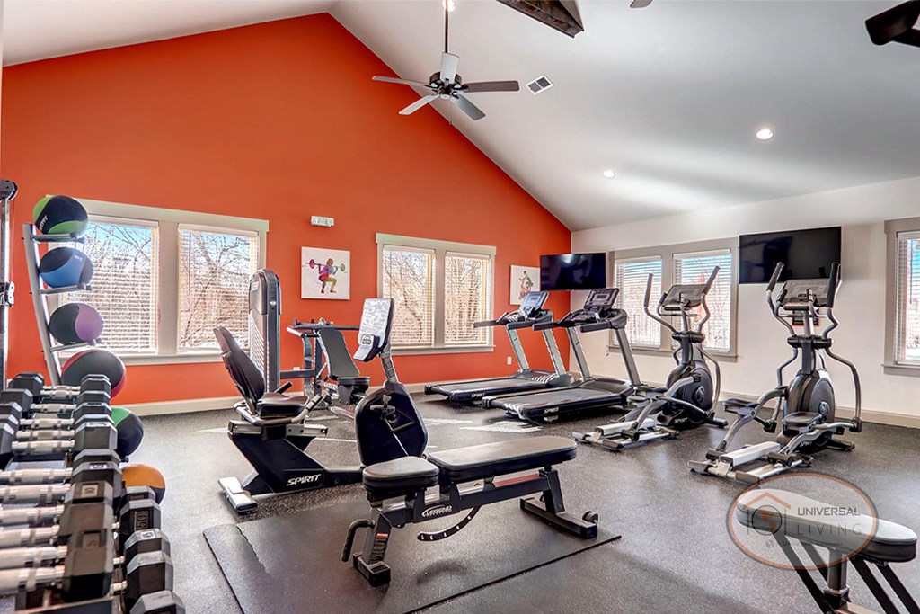 Universal at Lakewood, Apartment community in Hendersonville, NC - Fitness Center A fitness center with a wall of mirror and an orange accent wall, featuring weight training equipment and cardio equipment.