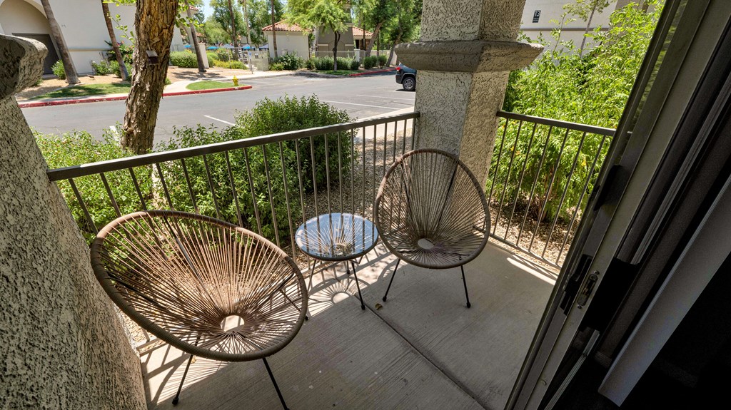 Two chairs are on a balcony with a table between them.