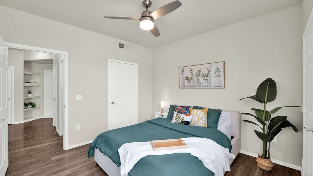A bedroom with a bed, a ceiling fan, and a potted plant.