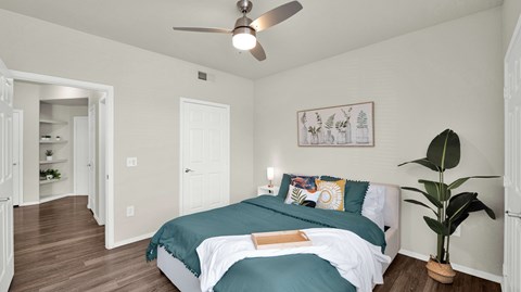 A bedroom with a bed, a ceiling fan, and a potted plant.