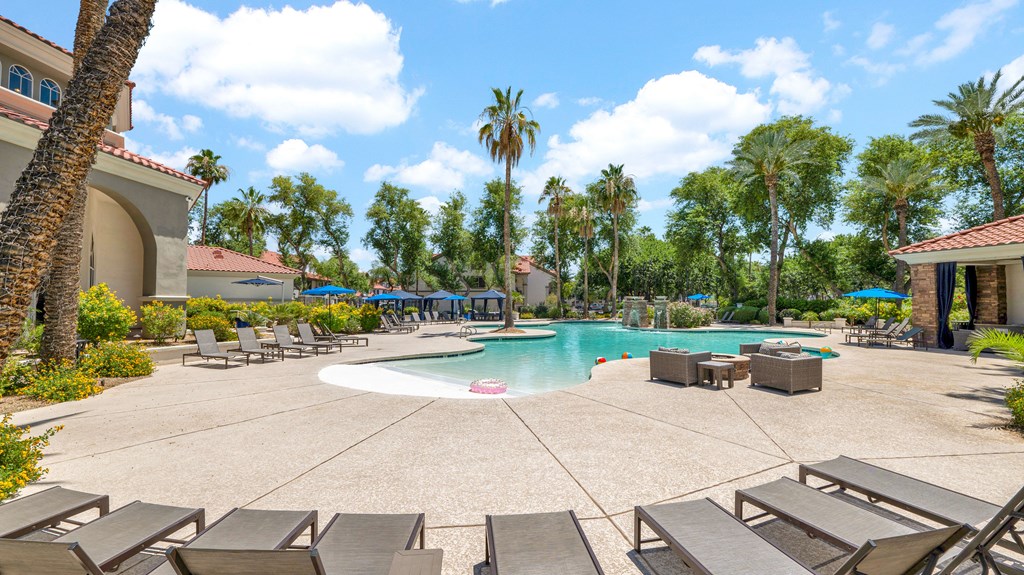 A large outdoor swimming pool surrounded by lounge chairs and palm trees.