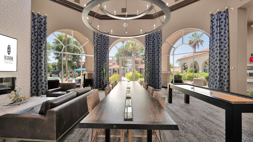 A long wooden table is in the middle of a room with a view of the outside.