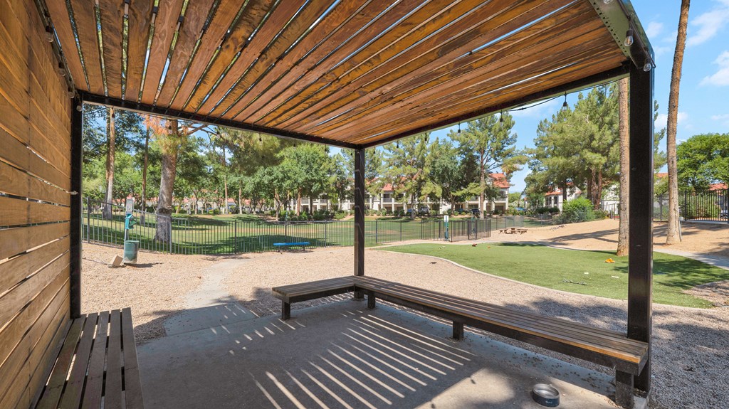 A wooden bench under a wooden structure in a park.