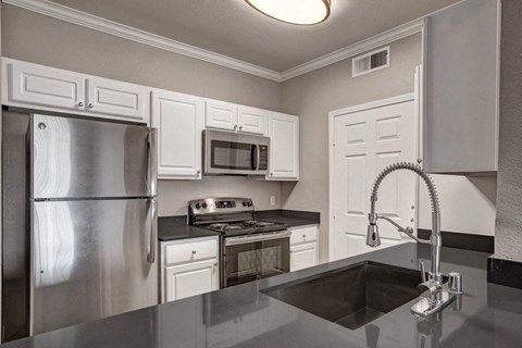 A kitchen with a stainless steel refrigerator and a black countertop.