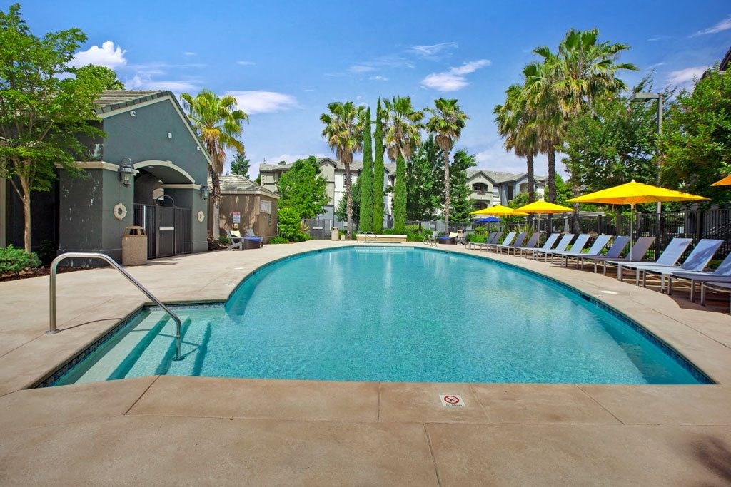 A large swimming pool with a metal ladder and yellow umbrellas in the background.
