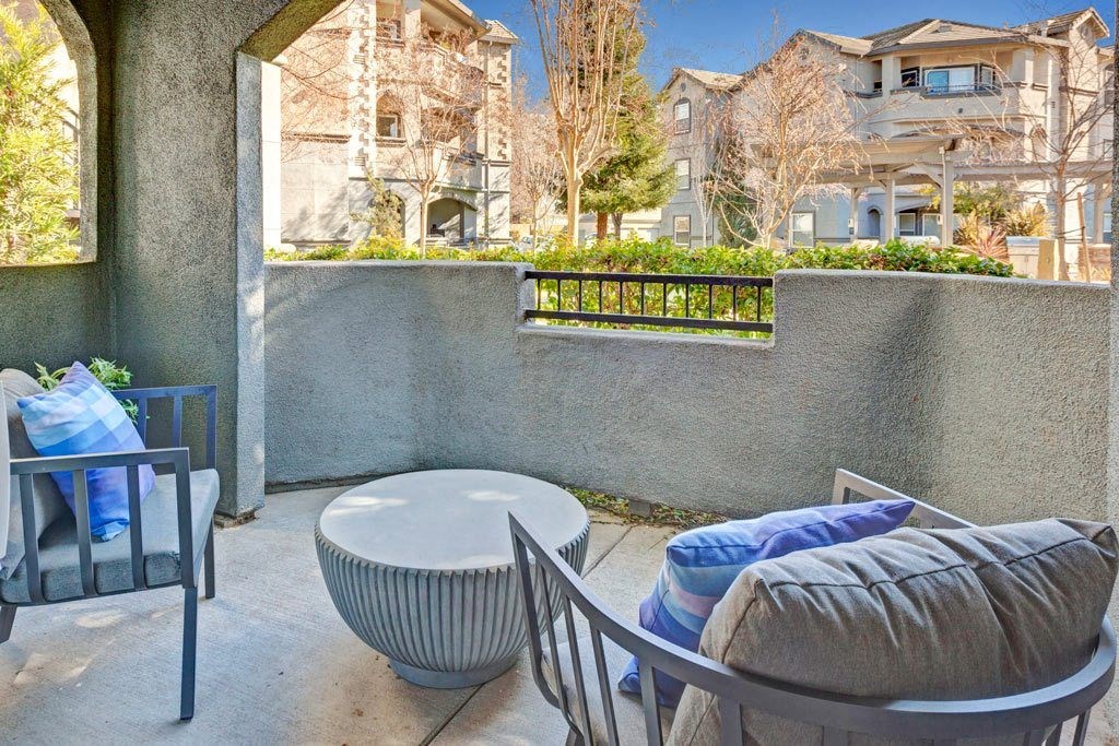 A patio with a chair, ottoman, and table with a view of apartment buildings.