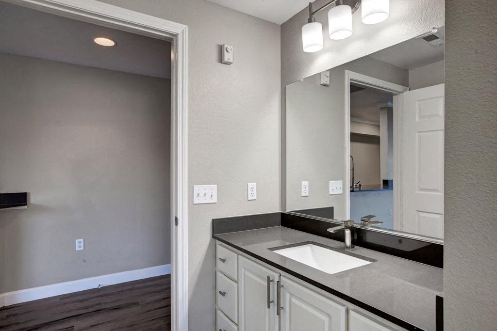 A bathroom with a sink, mirror, and light switches.
