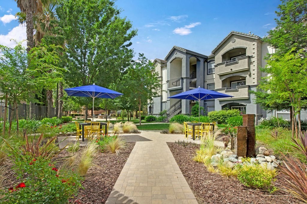 A walkway leads to a building with a blue umbrella on either side.